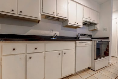 Kitchen with light tile patterned floors, white dishwasher, range, and white cabinets