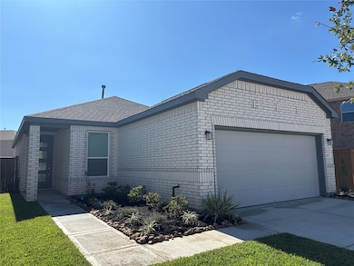 Modern single-story home with a light brick exterior, a two-car garage, and a tidy front yard with a small landscaped garden.