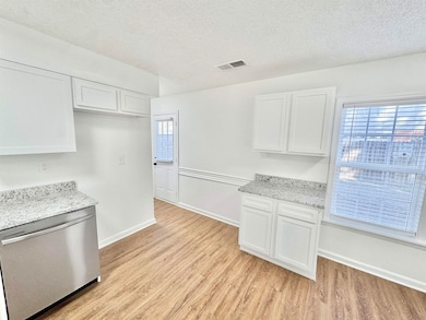 Kitchen featuring stainless steel dishwasher, light wood finished floors, white cabinets, a textured ceiling, and light stone counters