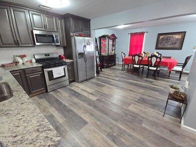 Kitchen featuring stainless steel appliances, light stone countertops, dark wood-style floors, and dark brown cabinetry