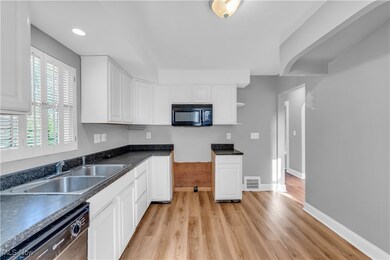 Kitchen with black microwave, dishwasher, light wood-style flooring, dark countertops, and white cabinets