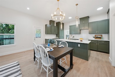 Kitchen featuring green cabinetry, decorative backsplash, light wood-style flooring, hanging light fixtures, and a kitchen island with sink