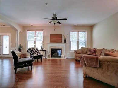 Living room with arched walkways, dark wood-style floors, ornate columns, ceiling fan, and a glass covered fireplace