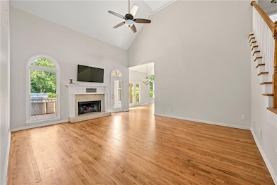 Unfurnished living room with a tile fireplace, a ceiling fan, light wood finished floors, high vaulted ceiling, and stairs