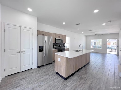 Kitchen featuring stainless steel appliances, a sink, ceiling fan, light countertops, and wood finish floors