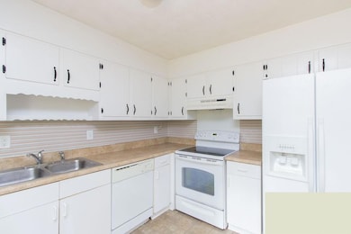 Kitchen featuring white appliances, under cabinet range hood, white cabinets, and light countertops