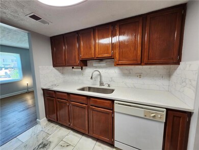 Kitchen featuring white dishwasher, light countertops, tasteful backsplash, and light marble finish flooring