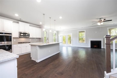 Kitchen with stainless steel appliances, crown molding, dark wood-style flooring, white cabinetry, and light stone counters