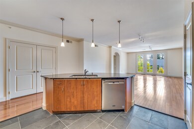 Kitchen with brown cabinetry, crown molding, dark stone countertops, arched walkways, and decorative light fixtures
