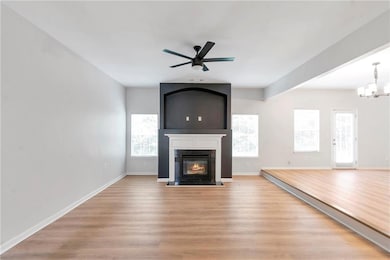 Unfurnished living room with ceiling fan, light wood finished floors, healthy amount of natural light, and a fireplace with flush hearth