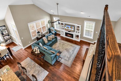Living room with ceiling fan, a glass covered fireplace, wood finished floors, baseboards, and high vaulted ceiling