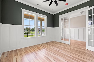 Empty room featuring a decorative wall, a ceiling fan, wood finished floors, a wainscoted wall, and ornamental molding
