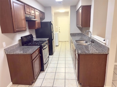 Kitchen featuring gas stove, light tile patterned floors, dark stone countertops, under cabinet range hood, and washer / dryer