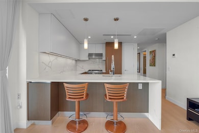 Kitchen with modern cabinets, a peninsula, light stone counters, backsplash, and pendant lighting
