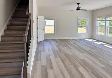 Unfurnished living room featuring a ceiling fan, wood finished floors, stairs, and baseboards