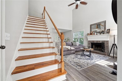 Staircase with a high ceiling, ceiling fan, wood finished floors, and a fireplace