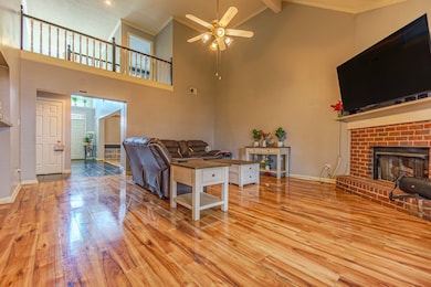 Living area with a brick fireplace, crown molding, light wood-style floors, ceiling fan, and beam ceiling
