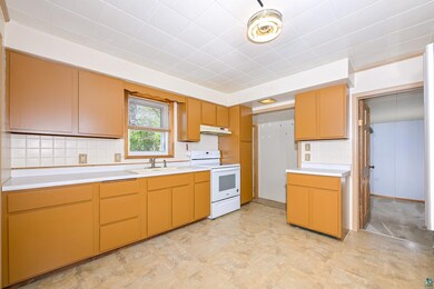 Kitchen with white electric range oven, a sink, light countertops, under cabinet range hood, and decorative backsplash