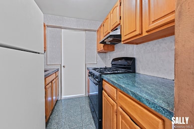 Kitchen featuring freestanding refrigerator, black gas range, granite floors, under cabinet range hood, and backsplash