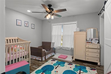 Bedroom with a barn door, ceiling fan, dark hardwo