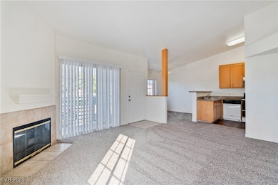 Unfurnished living room with light colored carpet, a tiled fireplace, and lofted ceiling