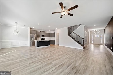 Unfurnished living room with ceiling fan with notable chandelier, recessed lighting, light wood-style flooring, and stairs