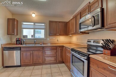 Kitchen with appliances with stainless steel finishes, a textured ceiling, light countertops, brown cabinetry, and light tile patterned flooring