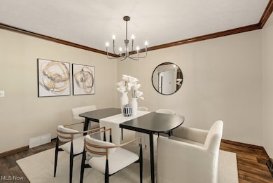 Dining room featuring dark wood-style flooring, ornamental molding, and a chandelier
