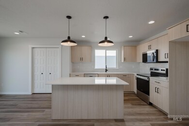 Kitchen with light brown cabinetry, stainless steel appliances, modern cabinets, decorative light fixtures, and backsplash