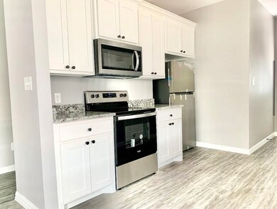 Kitchen with appliances with stainless steel finishes, white cabinetry, light wood finished floors, and light stone countertops