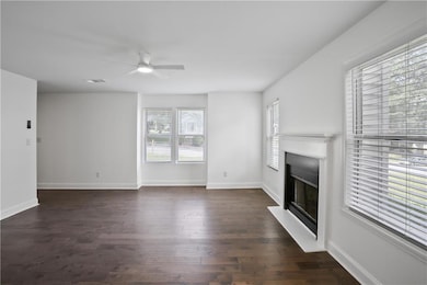 Unfurnished living room featuring a glass covered fireplace, dark wood-style flooring, and ceiling fan