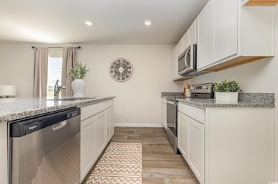 Kitchen featuring appliances with stainless steel finishes, white cabinetry, light stone countertops, light wood-style floors, and recessed lighting
