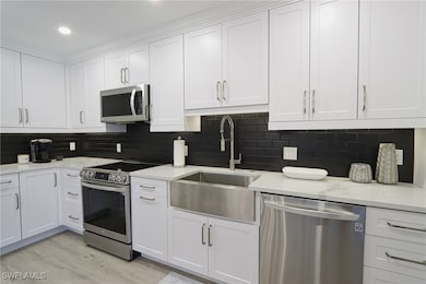 Kitchen with appliances with stainless steel finishes, a sink, white cabinetry, light wood-type flooring, and recessed lighting