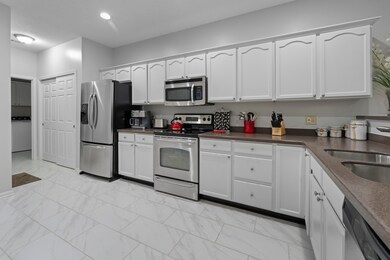 Kitchen featuring appliances with stainless steel finishes, light marble finish floors, washer / dryer, dark countertops, and white cabinets