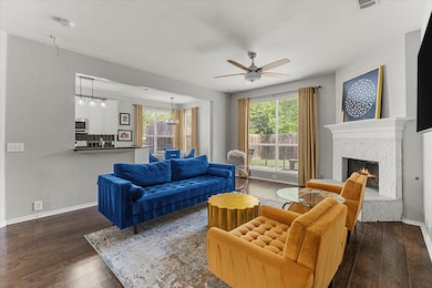 Living room with a ceiling fan, wood finished floors, and a lit fireplace