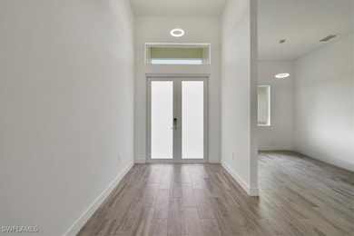 Foyer with wood finished floors, baseboards, a towering ceiling, and french doors