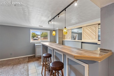 Kitchen featuring a kitchen breakfast bar, track lighting, crown molding, butcher block counters, and hanging light fixtures