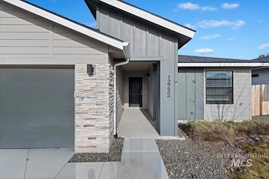 Entrance to property featuring stone siding, board and batten siding, a garage, and a shingled roof