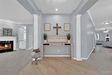 Hall featuring light colored carpet, crown molding, ornate columns, and light wood-style floors