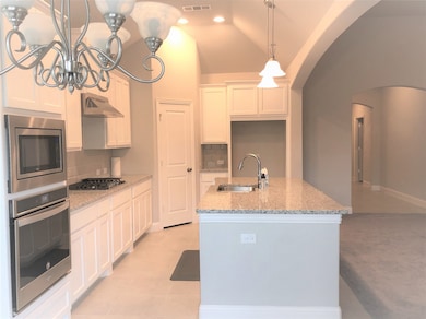 Kitchen with light stone countertops, a kitchen island with sink, decorative backsplash, appliances with stainless steel finishes, and white cabinetry