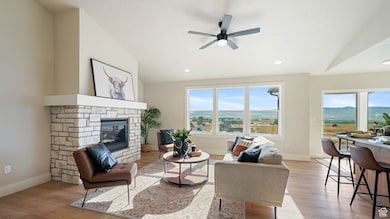Living area featuring light wood-type flooring, a ceiling fan, a stone fireplace, vaulted ceiling, and recessed lighting