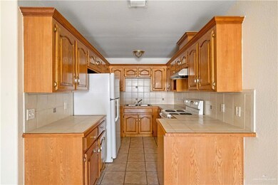 Kitchen with backsplash, white appliances, light tile patterned flooring, tile counters, and brown cabinets