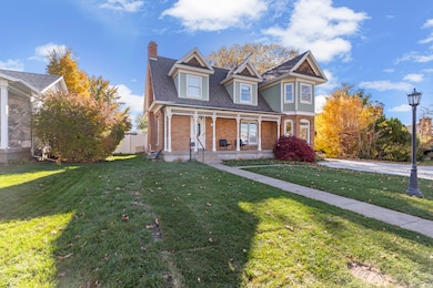 Victorian house featuring a porch, brick siding, a front lawn, a chimney, and roof with shingles
