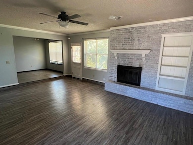 Unfurnished living room with a textured ceiling, a ceiling fan, dark wood finished floors, ornamental molding, and a fireplace