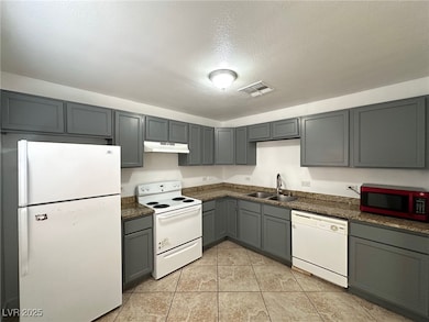 Kitchen featuring gray cabinets, white appliances, a textured ceiling, light tile patterned floors, and under cabinet range hood
