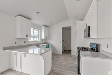 Kitchen with vaulted ceiling, a breakfast bar area, gas range oven, white cabinets, and a peninsula