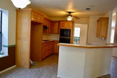 Kitchen featuring a peninsula, light countertops, a ceiling fan, black appliances, and light wood finished floors