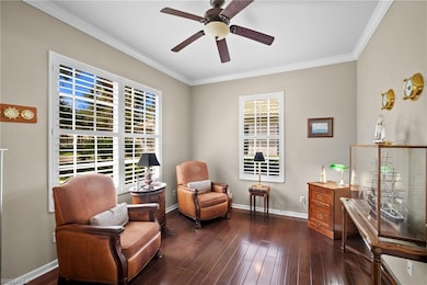 Living area with crown molding, dark wood finished floors, and a ceiling fan