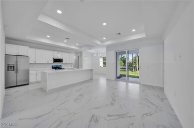 Kitchen with a raised ceiling, appliances with stainless steel finishes, open floor plan, white cabinets, and an island with sink