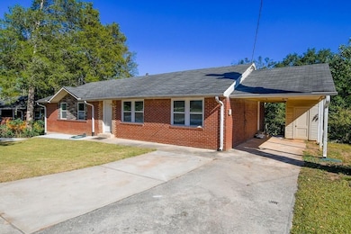 Single story home featuring a front lawn, an attached carport, driveway, brick siding, and a shingled roof